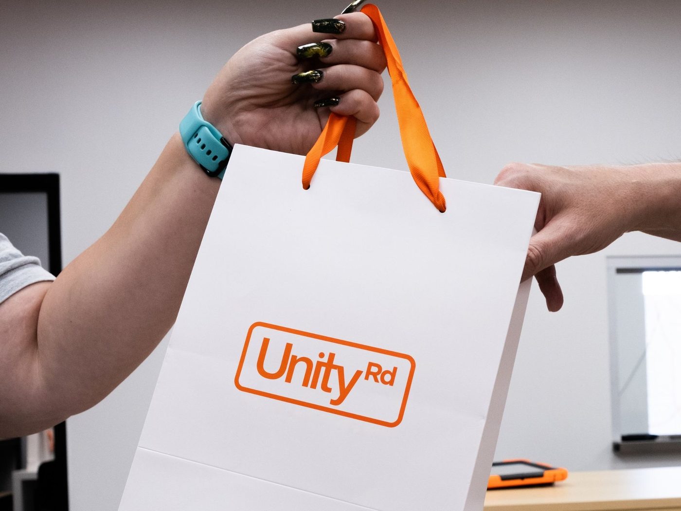 A Unity Rd. team member handing a customer a white Unity Rd. shopping bag with orange ribbon handles